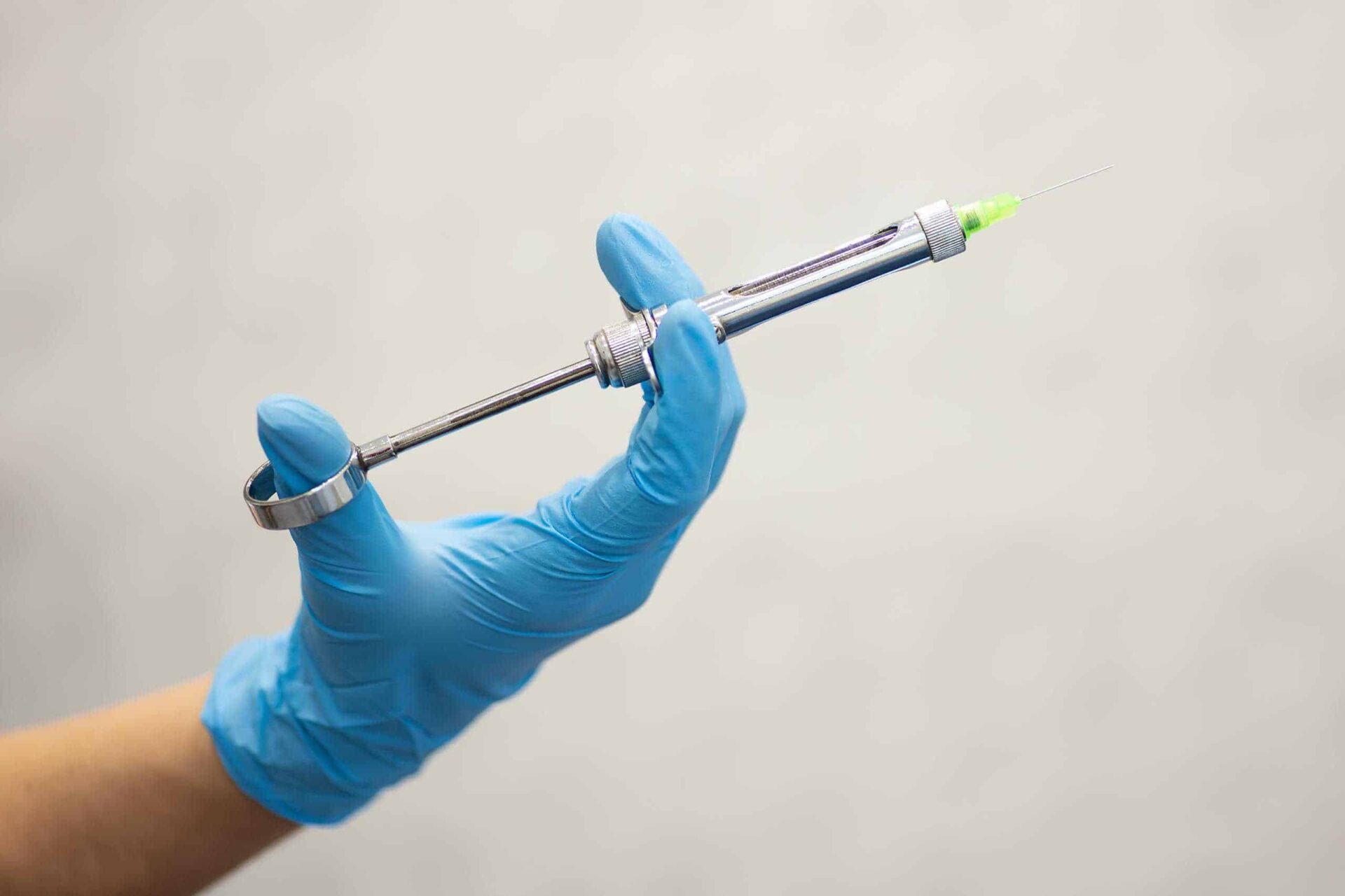 Gloved hand holding a metal dental anaesthetic syringe with the needle attached