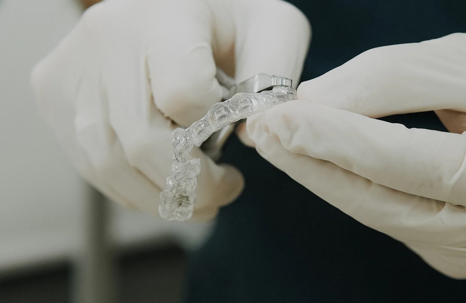 A woman fitting a clear aligner over her teeth with one hand while holding a second aligner in the other