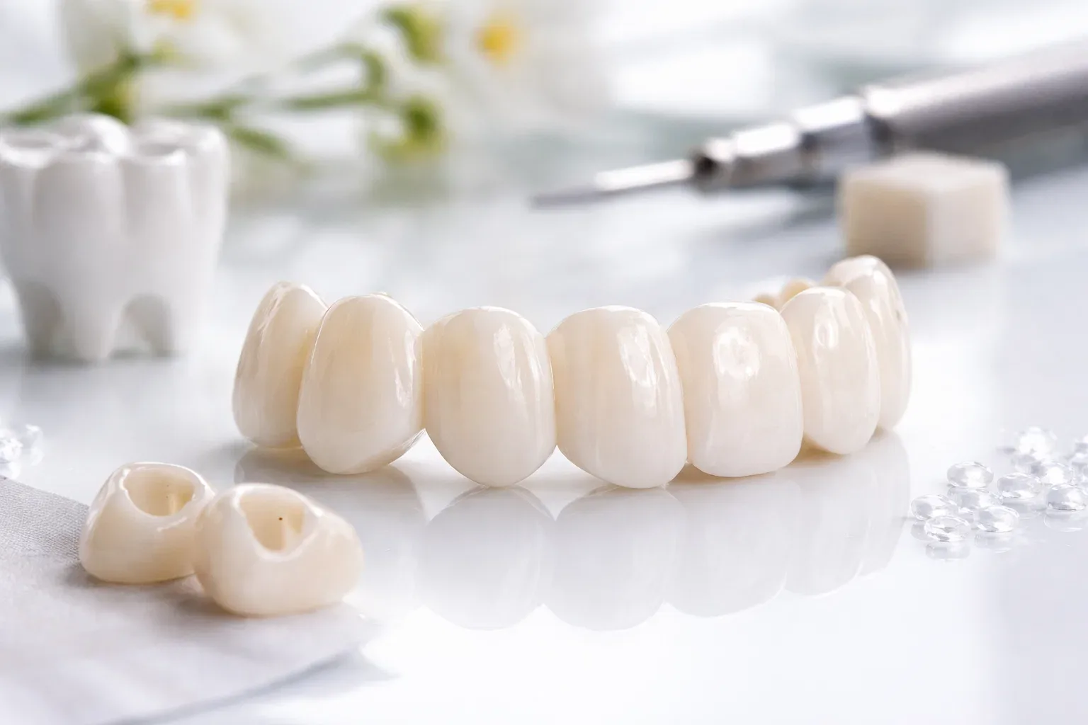 Multi-unit ceramic bridge on a white table, two single crowns in front and a molar model behind